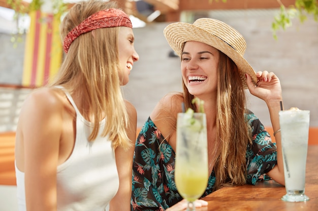 Mulheres bonitas se divertem juntas no café, bebem coquetéis frescos. mulheres adoráveis relaxadas relaxam durante as férias de verão.