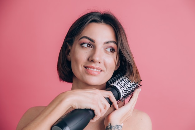 Mulheres com fundo rosa segurando uma escova redonda para pentear o cabelo