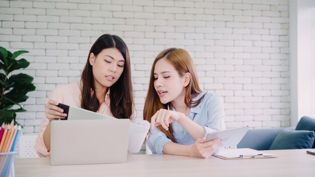 Mulheres de negócios asiáticos criativos inteligentes atraentes em casual desgaste inteligente trabalhando no laptop enquanto está sentado