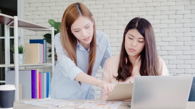 Mulheres de negócios asiáticos criativos inteligentes atraentes em casual desgaste inteligente trabalhando no laptop enquanto está sentado