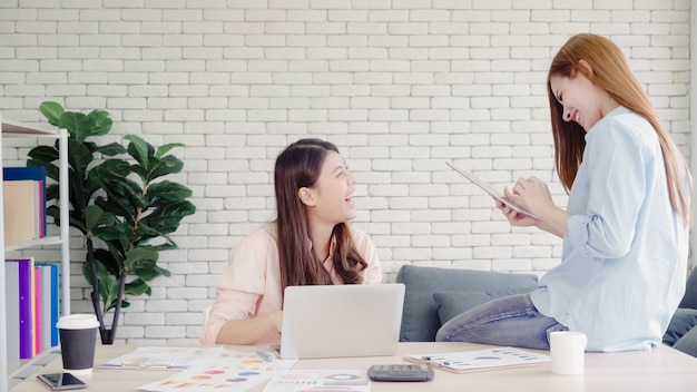 Mulheres de negócios asiáticos criativos inteligentes atraentes em casual desgaste inteligente trabalhando no laptop enquanto está sentado