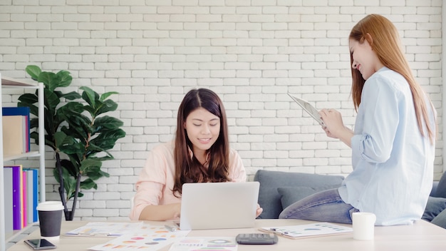 Mulheres de negócios asiáticos criativos inteligentes atraentes em casual desgaste inteligente trabalhando no laptop enquanto está sentado