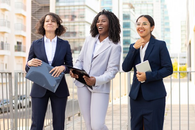 Mulheres de negócios com papéis e dispositivo digital. Colegas fêmeas multi-étnicos que mantêm o PC e os papéis da tabuleta exteriores. Conceito de negócios