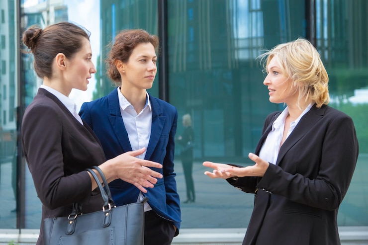 Foto grátis mulheres de negócios confiantes, discutindo projeto emocionalmente ao ar livre. colegas de trabalho vestindo ternos juntos na cidade e conversando.