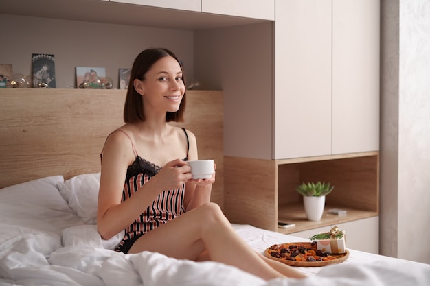 Mulheres desfrutando de café com marshmallows na cama com um presente perto dela. surpresa matinal