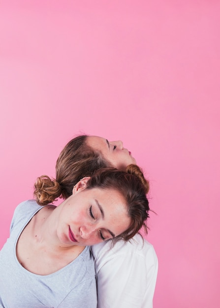 Mulheres dormindo no ombro do outro contra o fundo rosa