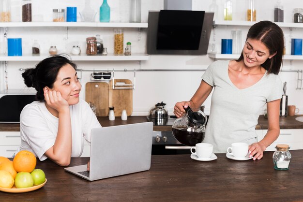 Mulheres em casa na cozinha com café e laptop