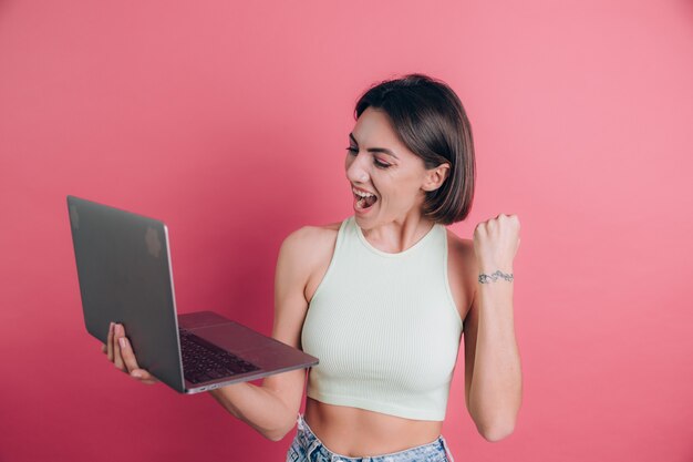 Mulheres em um gesto vencedor com um fundo rosa segurando um laptop