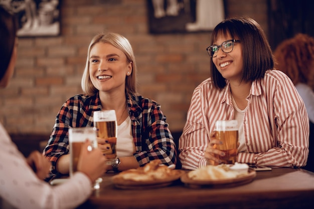 Mulheres felizes se comunicando enquanto bebem cerveja e relaxam em uma taverna