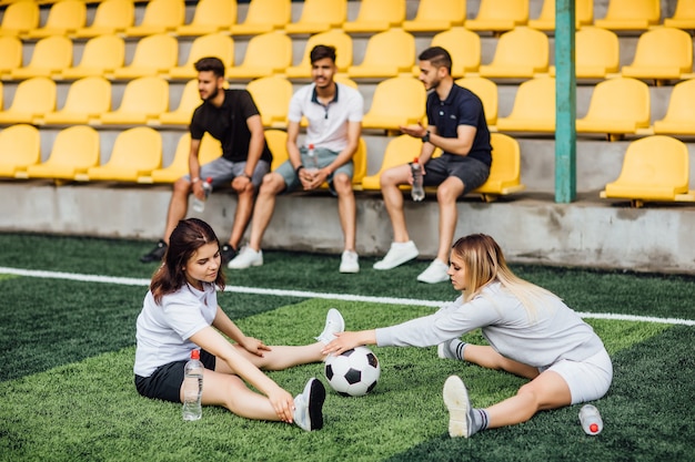 Mulheres jogadoras de futebol alongando os músculos da perna se preparando para a partida no estádio