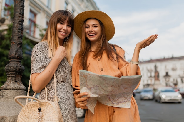 Mulheres jovens elegantes viajando juntas pela Europa usando vestidos e acessórios da moda para a primavera
