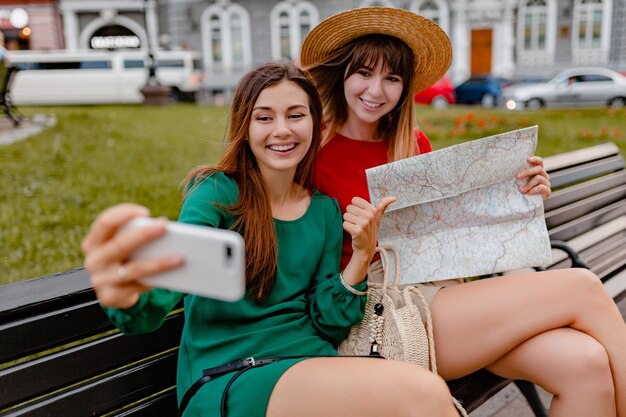 Mulheres jovens elegantes viajando juntas pela Europa usando vestidos e acessórios da moda para a primavera