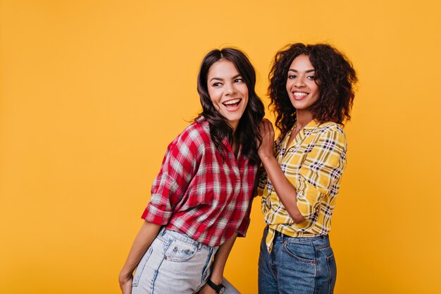 Mulheres jovens felizes dançando. Retrato dentro de casa de duas meninas elegantes em jeans.