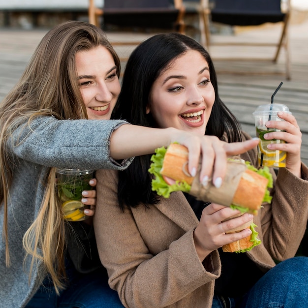 Mulheres jovens tomando sanduíches e coquetéis