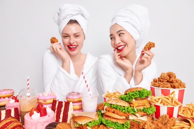 Mulheres mestiças felizes se olham com alegria, comem junk food, seguram nuggets, jantam saborosos