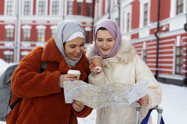 Mulheres muçulmanas com hijabs consultando um mapa e tomando café enquanto estão de férias