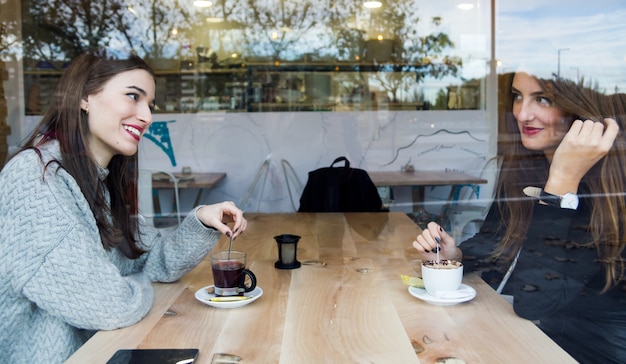 Mulheres novas bonitas que bebem o chá em uma cafetaria.