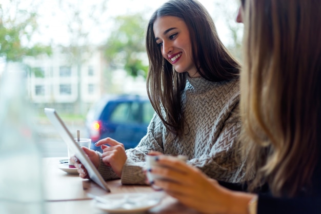 Mulheres novas bonitas que usam a tabuleta digital na cafetaria.