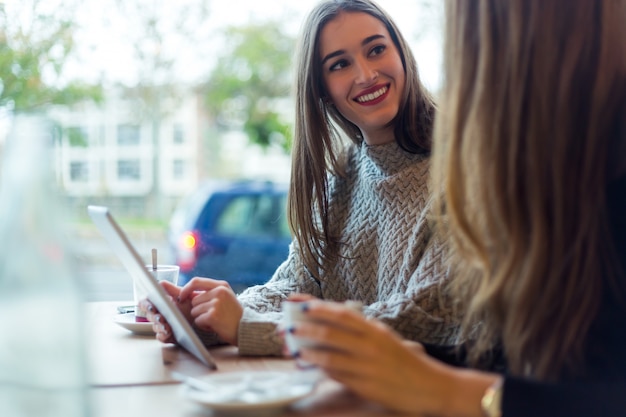 Mulheres novas bonitas que usam a tabuleta digital na cafetaria.