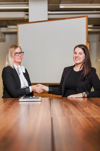 Mulheres sentadas à mesa apertando as mãos, sorrindo