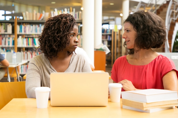 Mulheres sérias, sentado à mesa e usando o laptop