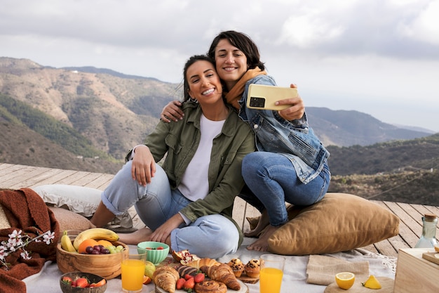 Mulheres sorridentes de tiro completo tomando selfie ao ar livre