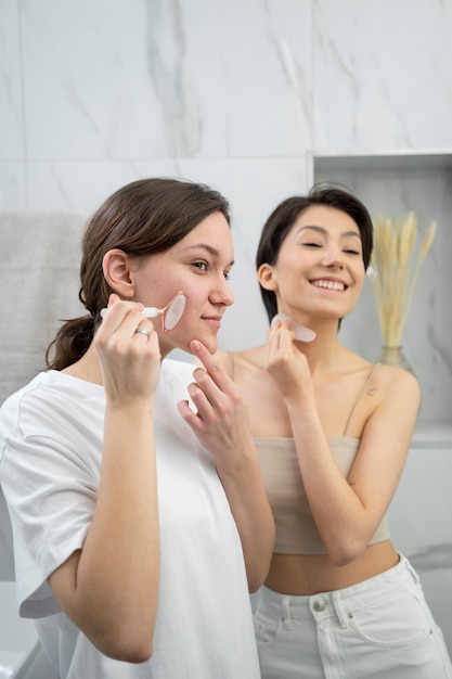 Mulheres sorridentes de tiro médio usando ferramentas gua sha