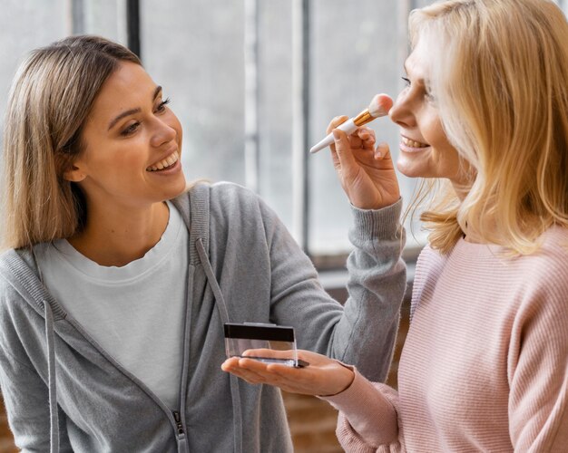 Mulheres sorridentes usando escova de maquiagem em casa