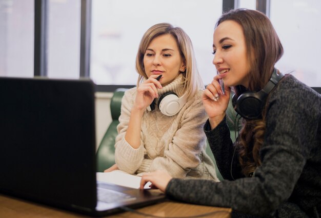 Mulheres usando fones de ouvido no pescoço olhando para laptop