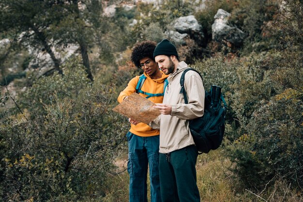 Multi étnico alpinista masculina olhando mapa na floresta