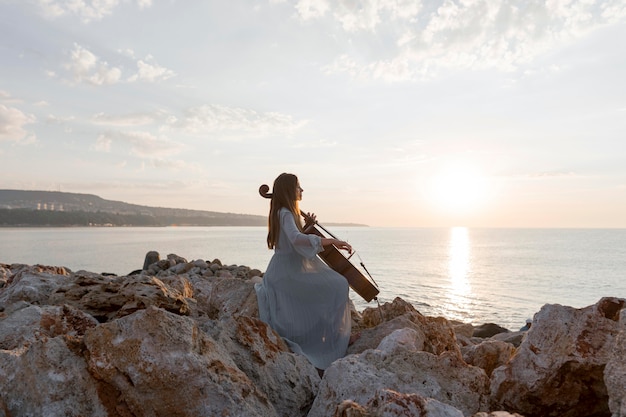 Música tocando violoncelo ao ar livre ao pôr do sol