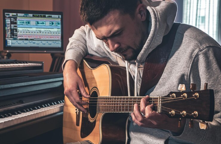 Foto grátis músico masculino toca guitarra em casa no local de trabalho perto do computador
