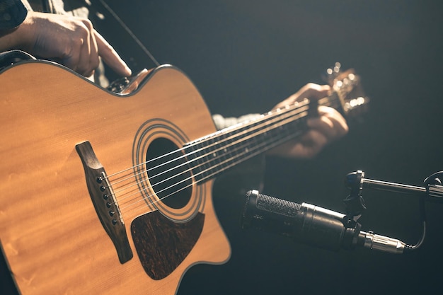 Foto grátis músico masculino tocando guitarra acústica atrás de um microfone em um estúdio de gravação