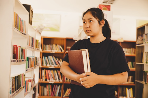 Na biblioteca - estudante jovem com livros que trabalham em uma biblioteca de ensino médio.