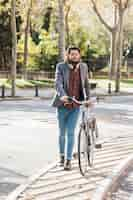 Foto grátis na moda jovem com fone de ouvido em volta do pescoço, andando com sua bicicleta na calçada