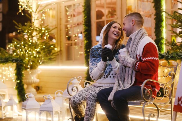 Na véspera de Natal, casal encantador de duas pessoas românticas está desfrutando de bebidas quentes enquanto está sentado no banco.