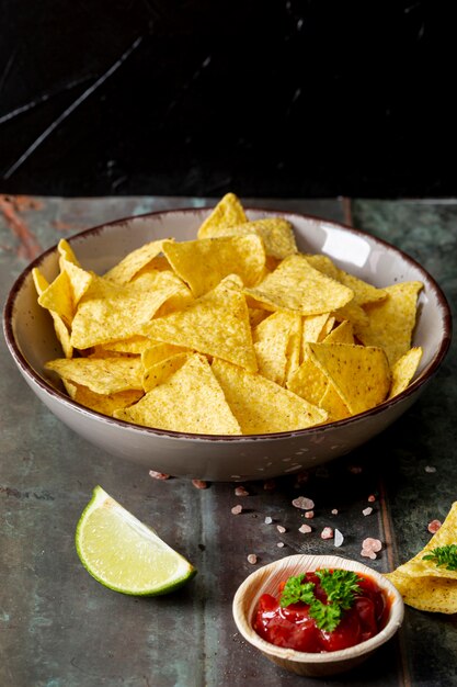 Nachos, molho de tomate e limão fatiado na mesa contra o fundo preto