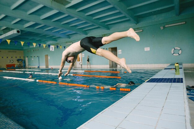 Nadador ativo pulando na piscina, início da competição. Piscina interior. Europeu.