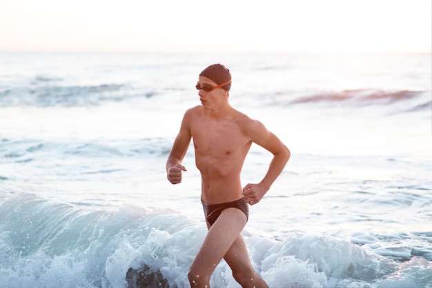 Nadador masculino com óculos e boné saindo do oceano