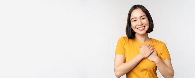 Namorada asiática romântica de mãos dadas no coração sorrindo com cuidado e ternura em amarelo