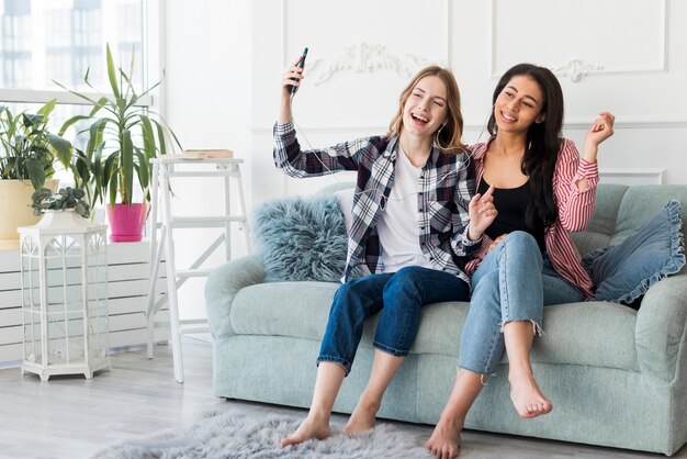 Namoradas, ouvindo música com fones de ouvido, sentado no sofá