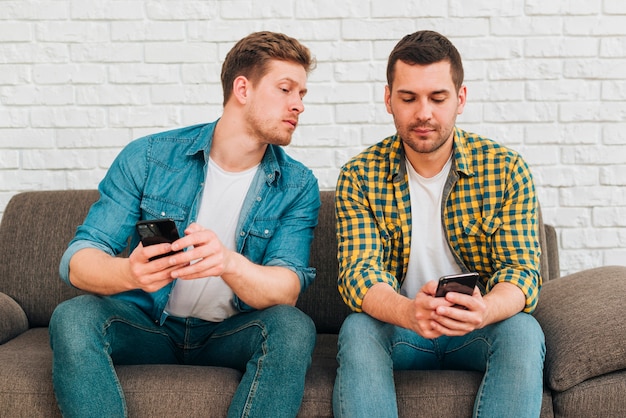 Foto grátis namorado ciumento espiando seu amigo masculino assistindo seu telefone