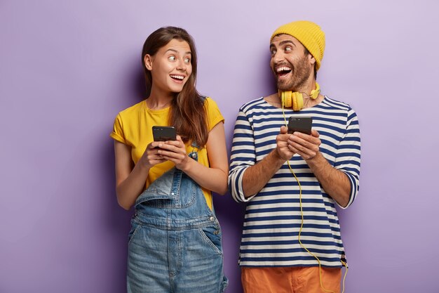 Namorado e namorada alegres riem e se olham, seguram telefones celulares