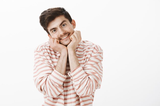 Namorado fofo charmoso com bigode, apoiando a cabeça nas mãos e sorrindo amigável, olhando com admiração, ouvindo atentamente a fala do atraente palestrante, em pé sobre a parede cinza