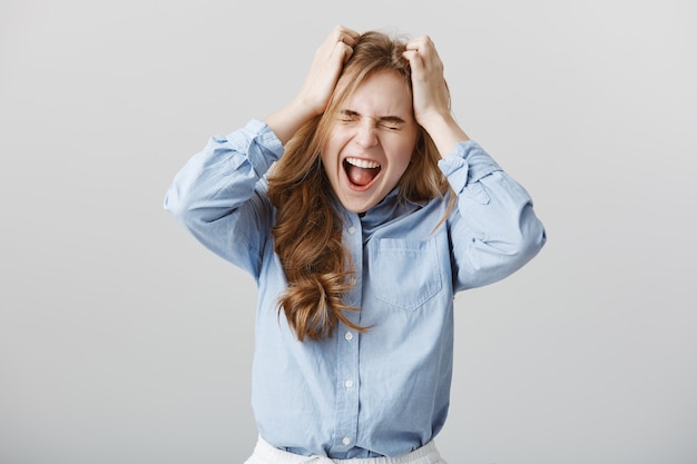 Foto grátis não aguento mais a pressão. modelo feminino europeu tensa e farta de camisa de colarinho azul, gritando ou gritando enquanto mantém as mãos na cabeça com os olhos fechados, sentindo dor ou sofrendo de depressão