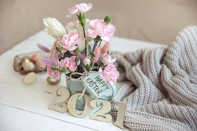 Natureza morta de páscoa com flores frescas da primavera em um vaso, tricotada com um elemento e número decorativo do ano 2021.