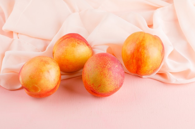 Foto grátis nectarina frescas na superfície rosa e têxtil, vista de alto ângulo.