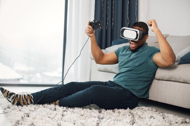 Negro com óculos de realidade virtual sentado em um tapete na sala de estar