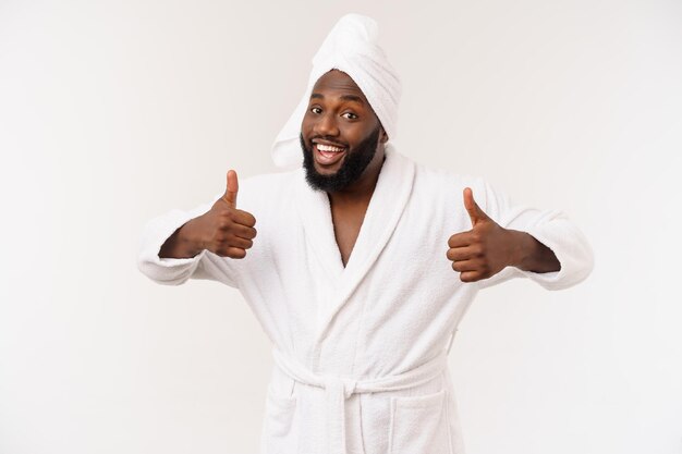 Negro vestindo um roupão de banho aparecendo polegar com surpresa e emoção feliz isolado sobre fundo branco