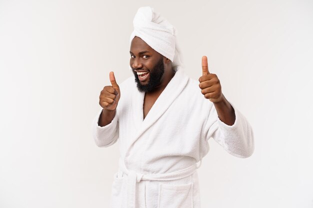 Negro vestindo um roupão de banho aparecendo polegar com surpresa e emoção feliz Isolado sobre fundo branco